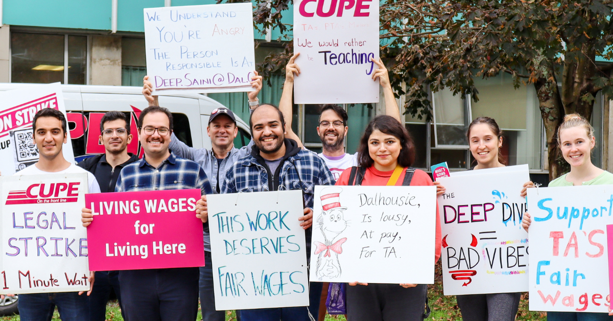 Group of CUPE 3912 members outdoors, holding picket signs in front of a building at Dalhousie University